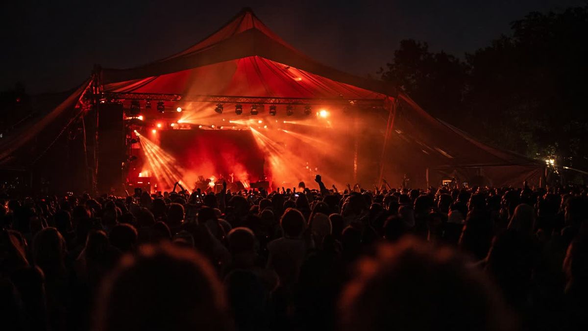 Festivalpodium onder een rood verlichte tent met publiek op de voorgrond: sfeerbeeld voor een eventvideo
